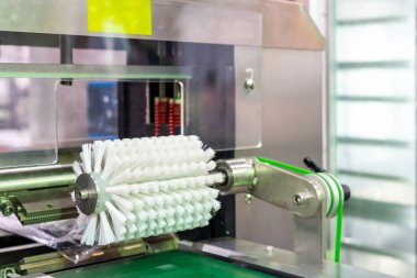 White pp roller brush on machine over bent conveyor component for cleaning product before next process such as contain and packing in food industrial or other