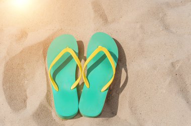 Yeşil ve sarı yaz terlikleri denizin kumlu sahilinde duruyor.