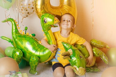 Altın, yeşil ve sarı balonlu bir doğum günü partisi için dekore edilmiş küçük çocuk, büyük şişme 4 numara, kutular ve kurdeleler sunar. Evdeki fotoşoplama alanı. Dinozor balonları.
