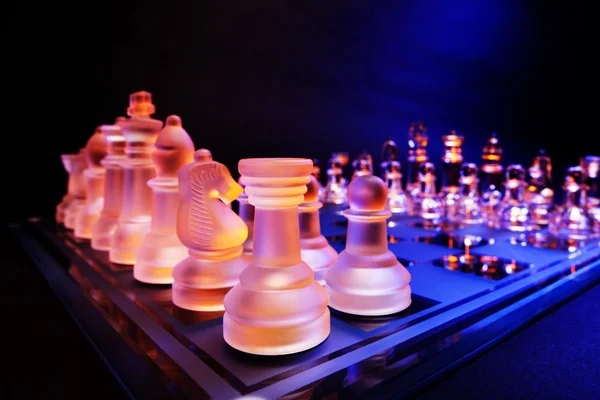 Glas chess på ett schackbräde upplyst av ett blått och orange ljus — Stockfoto