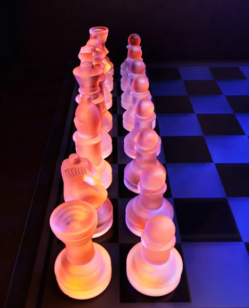 Szachy szklane na szachownicy oświetlony przez światło niebieskie i pomarańczowe — Zdjęcie stockowe