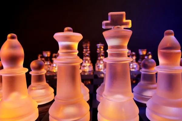 Glas chess på ett schackbräde upplyst av ett blått och orange ljus — Stockfoto