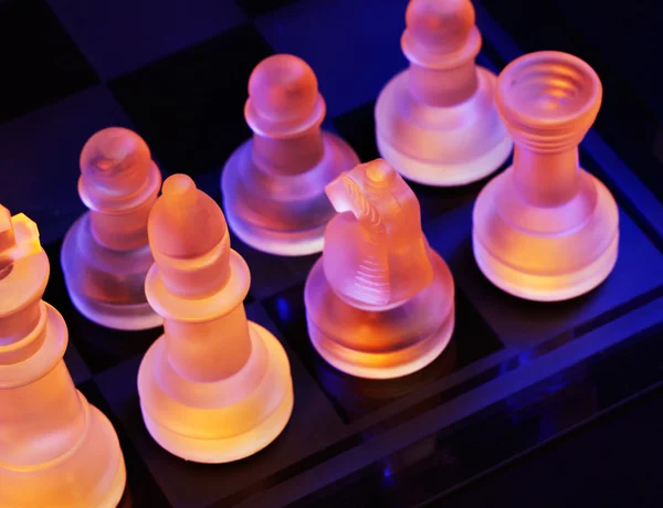 Xadrez de vidro em um tabuleiro de xadrez iluminado por uma luz azul e laranja — Fotografia de Stock
