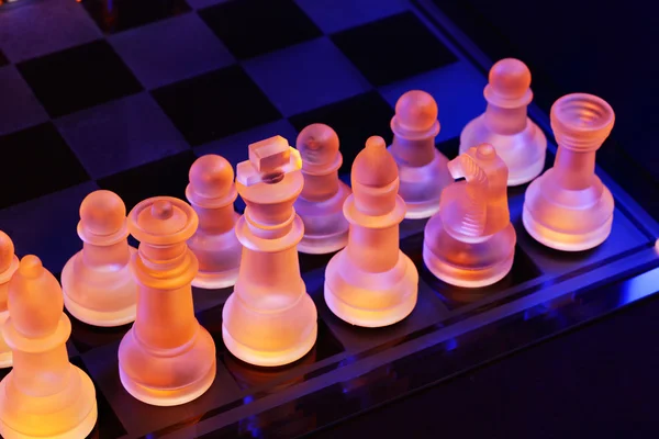 Glas chess på ett schackbräde upplyst av ett blått och orange ljus — Stockfoto