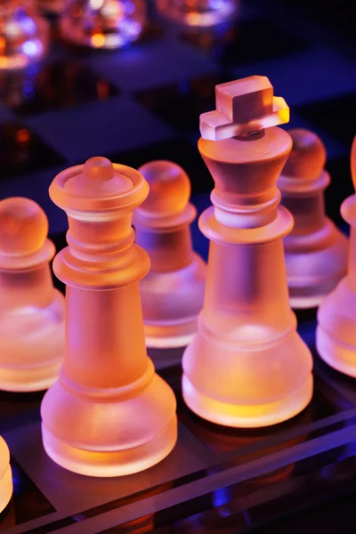 Glas chess på ett schackbräde upplyst av ett blått och orange ljus — Stockfoto