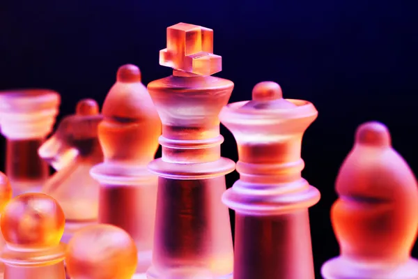 Échecs en verre sur un échiquier éclairé par une lumière bleue et orange — Photo