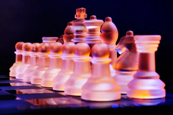 Glas chess på ett schackbräde upplyst av ett blått och orange ljus — Stockfoto