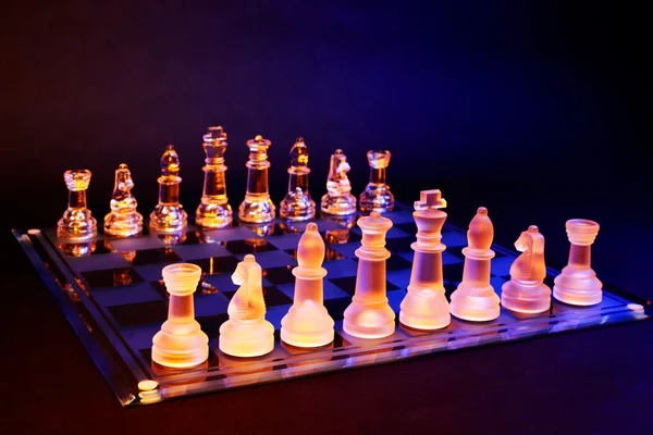 Échecs en verre sur un échiquier éclairé par une lumière bleue et orange — Photo