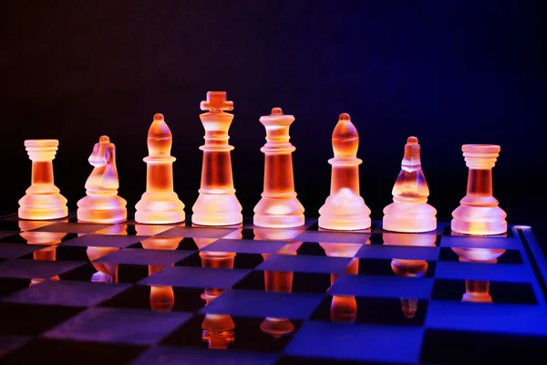 Szachy szklane na szachownicy oświetlony przez światło niebieskie i pomarańczowe — Zdjęcie stockowe