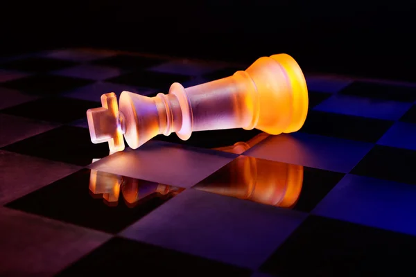 Glas chess på ett schackbräde upplyst av ett blått och orange ljus — Stockfoto