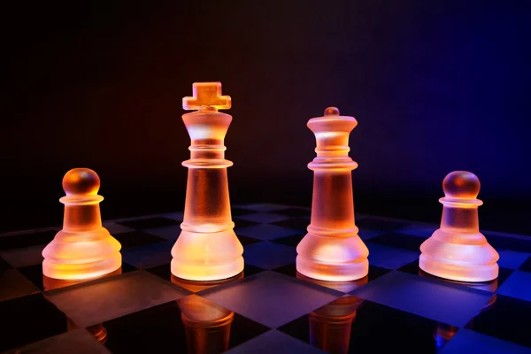 Échecs en verre sur un échiquier éclairé par une lumière bleue et orange — Photo