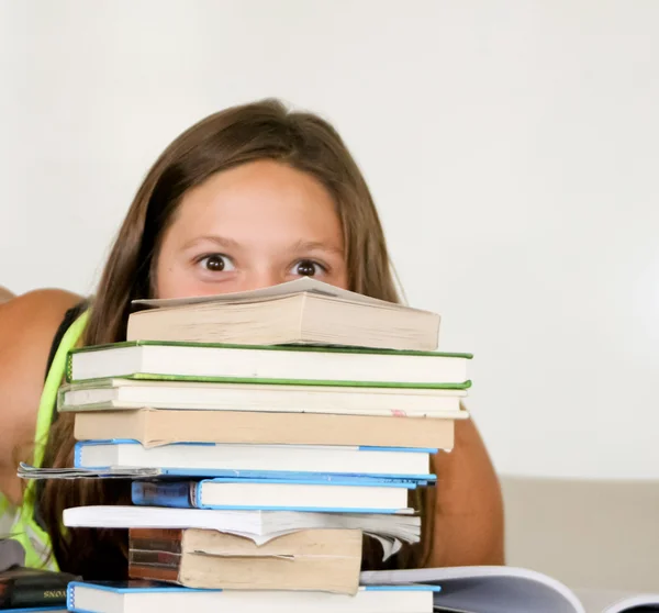 Adolescente estudiante hembra espiando sobre pila de libros — Foto de Stock