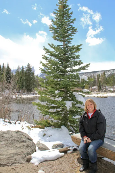 Senior female sitting by snowy lake — Stock Photo, Image