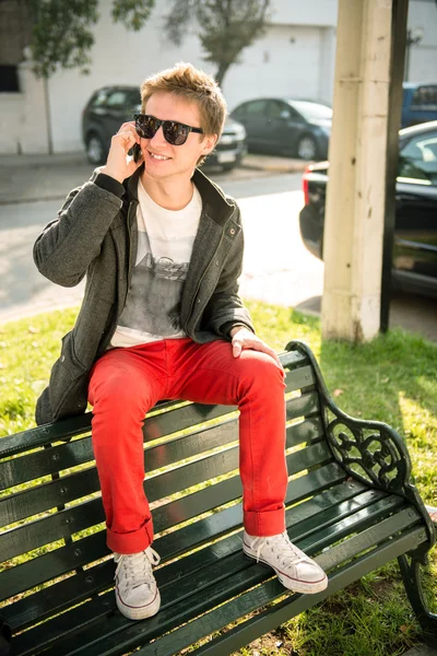 Un joven sentado en un banco hablando por teléfono — Foto de Stock