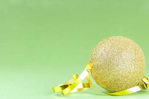 Golden ball with a golden ribbon on a green background. Christmas decorations. New Year. Christmas. Copy space. Bakcground