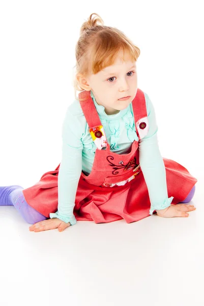 Ein kleines Mädchen in einem roten Kleid, sitzend in Pose — Stockfoto