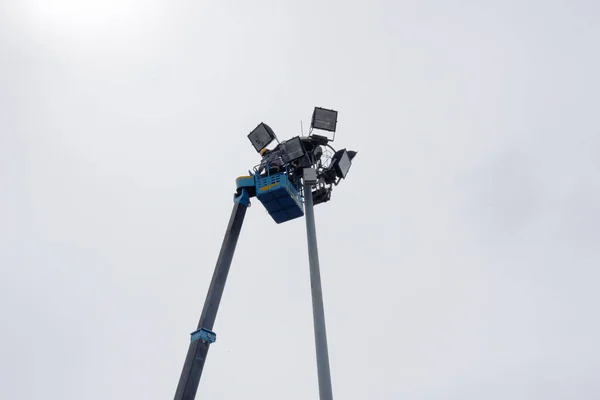 Workers equipped with helmets and safety equipment installed new diode lights. Workers in light poles repair lifting buckets