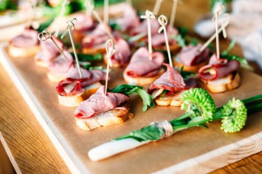 Delicious catering banquet buffet table decorated in rustic style in the garden. Different snacks, sandwiches with ham and greenery on a wooden plate. Outdoor.