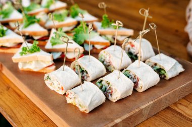 Delicious catering banquet buffet table decorated in rustic style in the garden. Different snacks, sandwiches with meat, greenery, eggs, cucumber and pesto sauce. Outdoor, closeup.