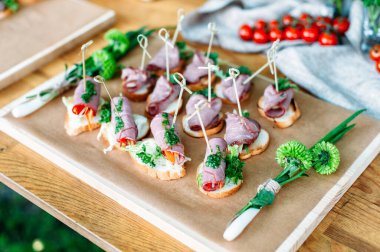 Delicious catering banquet buffet table decorated in rustic style in the garden. Different snacks, sandwiches with ham and pesto sauce. Outdoor, closeup.