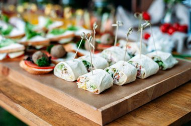 Delicious catering banquet buffet table decorated in rustic style in the garden. Different snacks, sandwiches with ham, vegetables and pesto sauce. Outdoor, closeup.