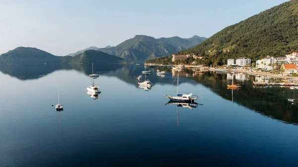 Aerial top drone view to the seashore and resorts in Marmatis, Turkey. Beach with sunbeds, umblrellas, palm trees, yachts and mountains on the background. Sunrise. Nobody. Wide angle.