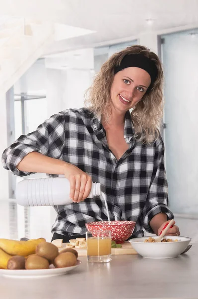 Sorrindo jovem mulher olhando para a câmera enquanto derramando leite em uma tigela para um delicioso café da manhã — Fotografia de Stock