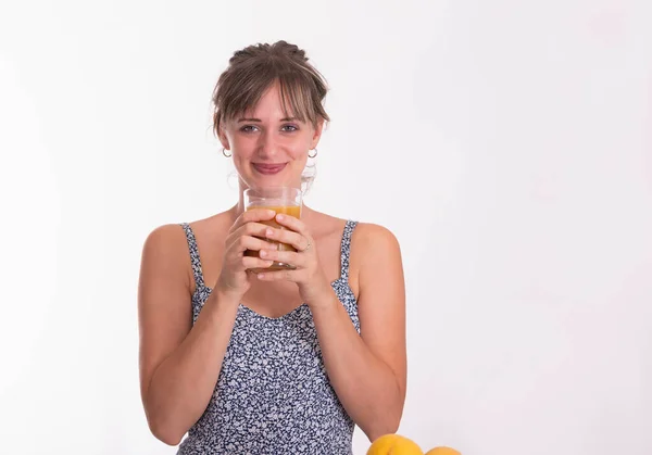 Улыбающаяся молодая женщина держит стакан фруктового сока обеими руками, глядя в камеру — стоковое фото