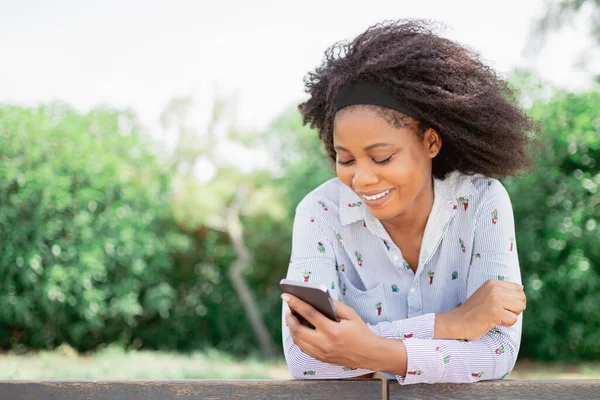Zicht op een vrolijke Afro-Amerikaanse vrouw glimlachend tijdens het gebruik van haar mobiele telefoon buiten. Stockfoto