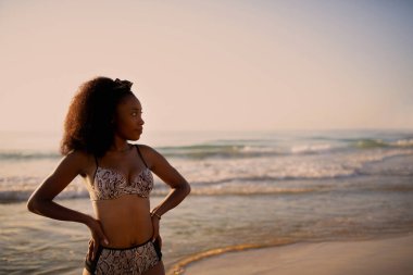 İki eli belinde duran bir kadın başka tarafa bakıyor.