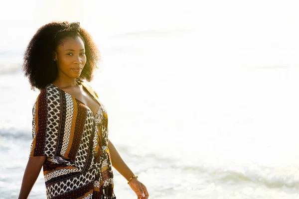 Afrikaanse vrouw glimlachend wandelen langs het strand en kijken naar camera — Stockfoto