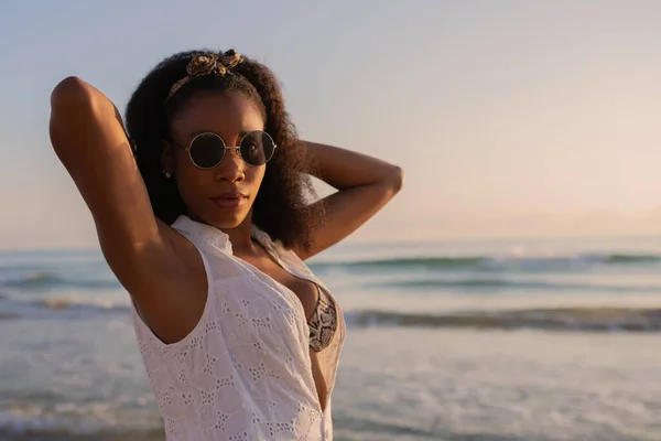 Vista recortada de una mujer con gafas de sol en la playa mirando a la cámara con ambas manos detrás de la cabeza — Foto de Stock