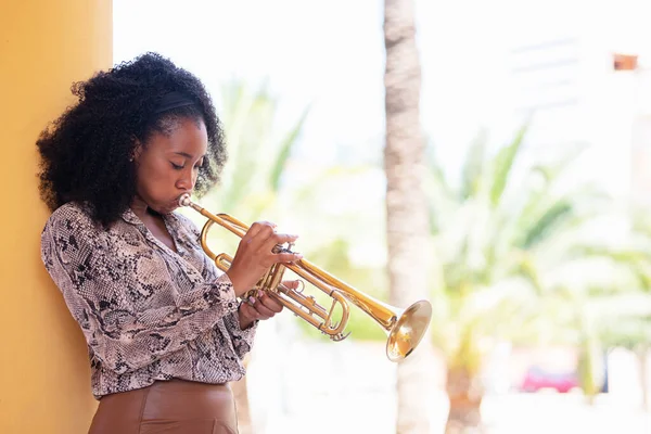 Mujer afroamericana concentrada apoyada en una columna de hormigón tocando la trompeta afuera — Foto de Stock