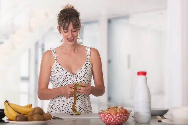 Mulher gesticulando com a boca enquanto descascando kiwis para o café da manhã nutritivo — Fotografia de Stock