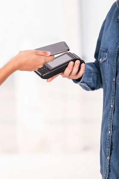 Side view of unrecognizable person paying with contactless payment by phone on white background.