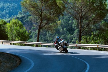 Well geared biker riding a motorcycle along a curve on an out of focus forest background. Selective focus. Driving and leisure concept.