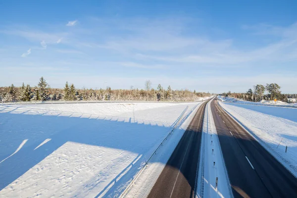 Mavi gökyüzünün arka planında, karlı bir otoyolda bir köprü ile güzel bir manzara. İsveç. 