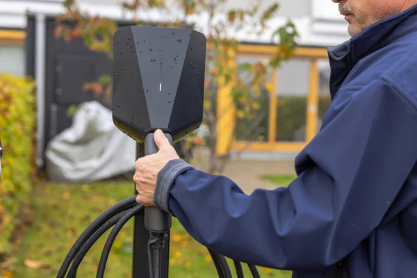 Şarj olan bir kabloyu bağlayan adamın yakın görüntüsü. Elektrikli araba için şarj eden bir araba istasyonu. İsveç. 