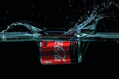 Siyah arkaplanda su izolasyonuna düşen Coca Cola kutusunun yakın görüntüsü. İsveç. Uppsala. 24.10.2021.