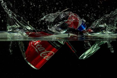 Coca Cola kutusunun yakın görüntüsü, pepsi kolanın siyah arkaplanda su izolasyonuna düşüşü. İsveç. Uppsala. 11.29.2021.