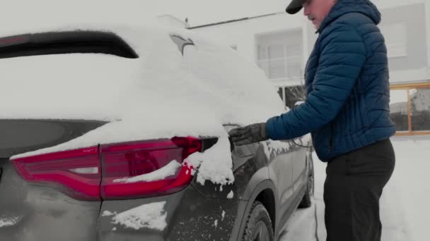 寒い冬の日に充電ケーブルを電気自動車充電ステーションに接続する男のビュー スウェーデン — ストック動画