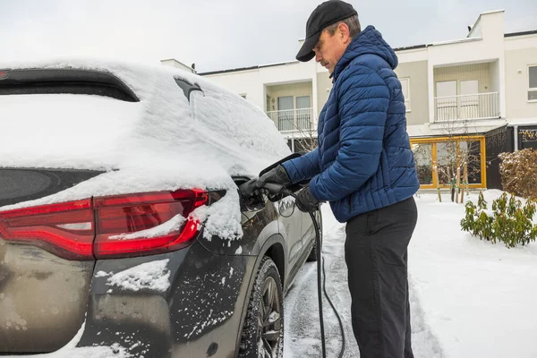 Soğuk bir kış gününde elektrik yüklü bir kabloyu elektrikli araba şarj istasyonuna bağlayan bir adamın güzel manzarası. İsveç.