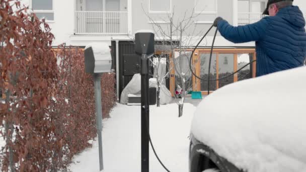 寒い冬の日に自宅の駐車場にある電気自動車充電ステーションから充電ケーブルを折り畳む男の眺め スウェーデン — ストック動画