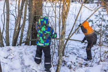 Karlı ormanda oynayan, renkli, sıcak kış kıyafetleri giymiş iki çocuğun güzel manzarası. İsveç. 