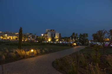 Otel alanının güzel gece manzarası. Işıklar, ağaçlar ve koyu mavi gökyüzü arka planındaki modern binalar. Yunanistan. 