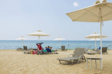 Beyaz kumlu Yunanistan plajının güzel manzarası. Güneş şemsiyeleri altında güneşli yataklar turkuaz su ve beyaz bulutlu mavi gökyüzü..  