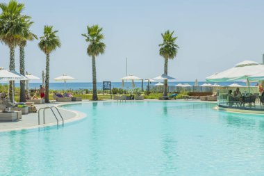 View of outdoor pool and people on sun beds and in pool bar on sunny summer day. Greece. Nea Potidaea. 09.03.2021.