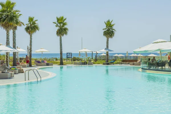View of outdoor pool and people on sun beds and in pool bar on sunny summer day. Greece. Nea Potidaea. 09.03.2021.