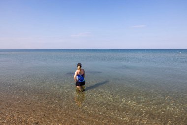 Sakin deniz suyunda duran ve ufka bakan kadının yakın görüntüsü. Yunanistan. 