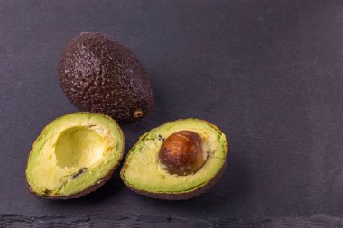 Kesik ve siyah kesme tahtasındaki tüm avokado meyvesinin yakın görüntüsü. Sağlıklı gıda konsepti. 